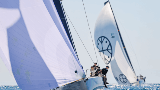 Two boats racing at Festival of Sails 2026, with crew sitting over the edge of one boat. Entries at open and how to enter information is now online for the 2027 event.
