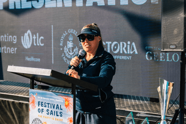 Sailor Girl Nic Douglass from Sunset Media stands in front of the podium with a microphone doing presentations at Festival of Sails 2026.